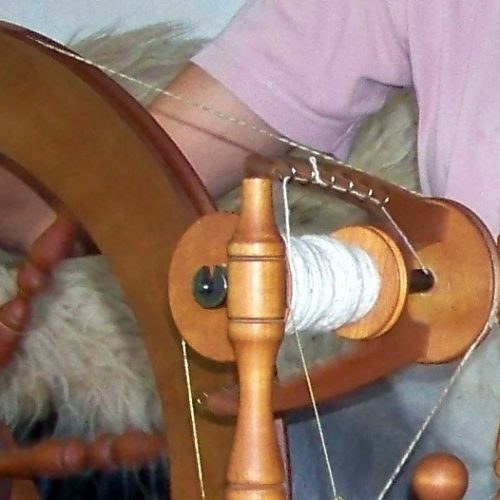 Bild zeigt ein Spinnrad, welches von einer Frau bedient wird.